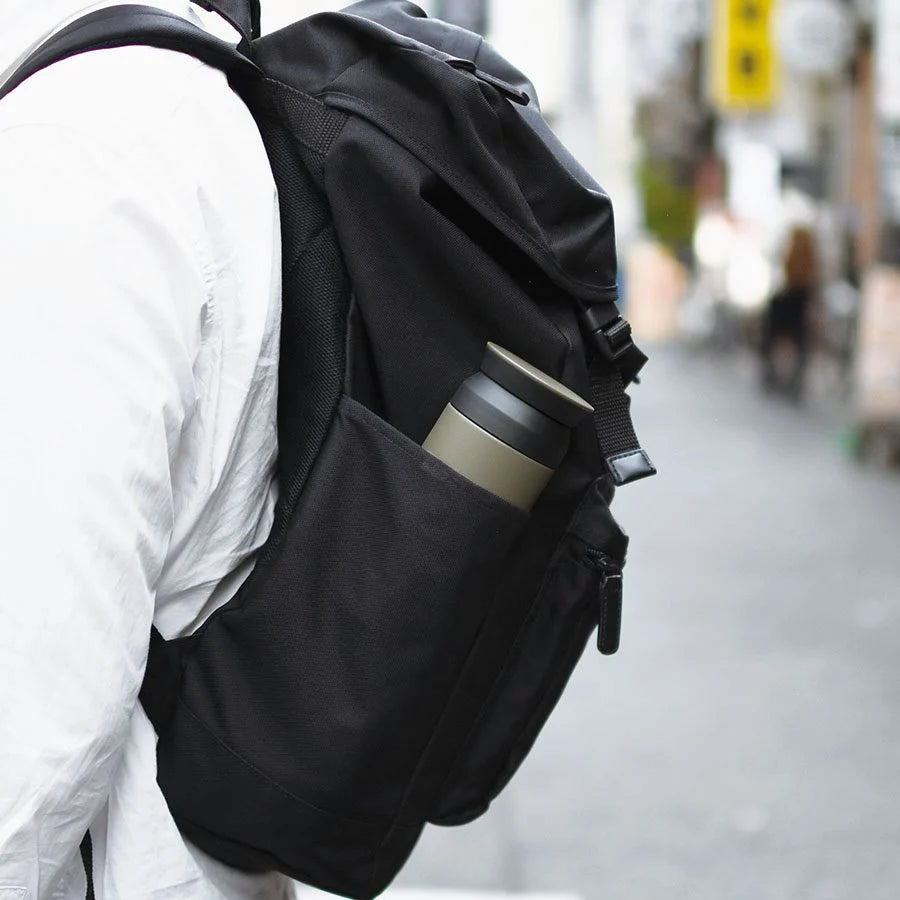 Black backpack with a water bottle on a blurred street background