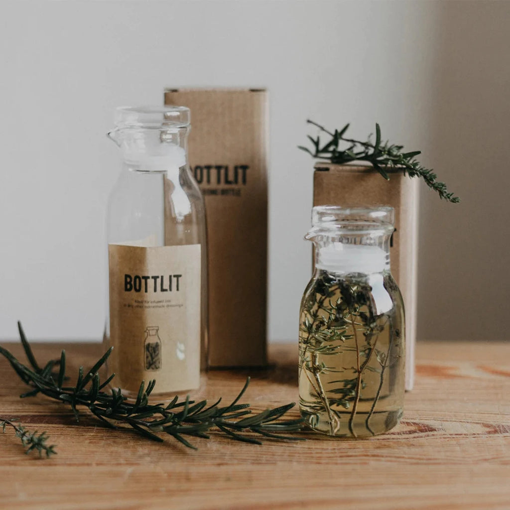 Two glass bottles withBOTTLIT branding on a wooden surface with greenery.