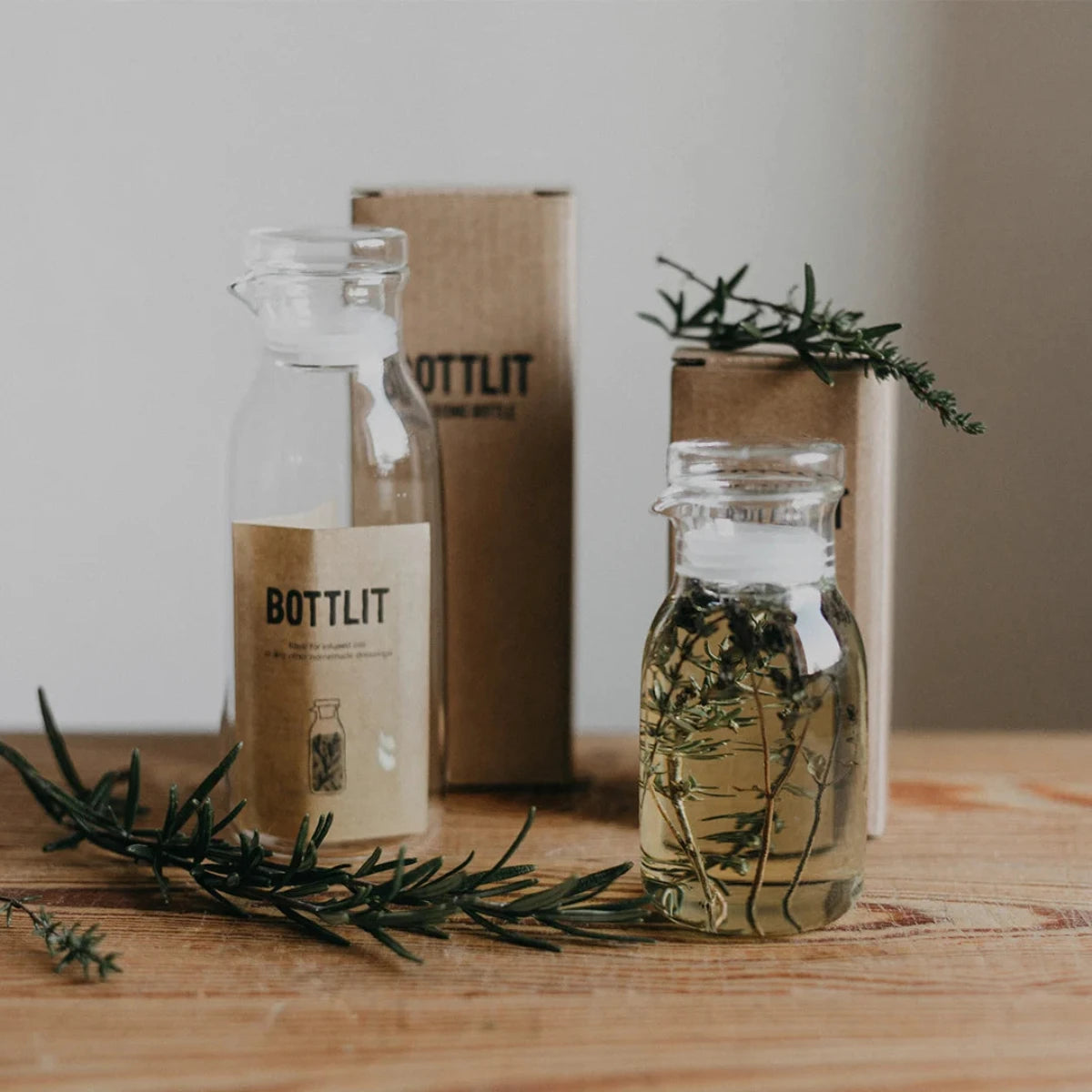Two glass bottles withBOTTLIT branding on a wooden surface with greenery.
