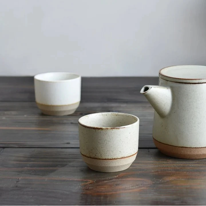 Ceramic teapot and two cups on a wooden surface with a plant in the background.