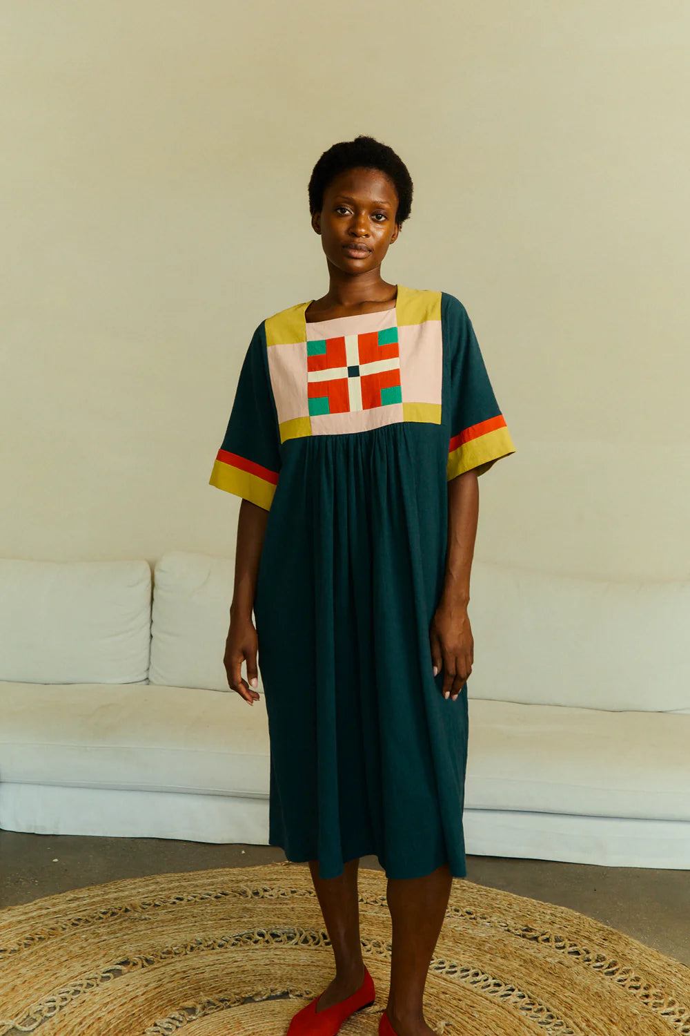 Woman wearing a colorful dress with geometric patterns in a minimal indoor setting.