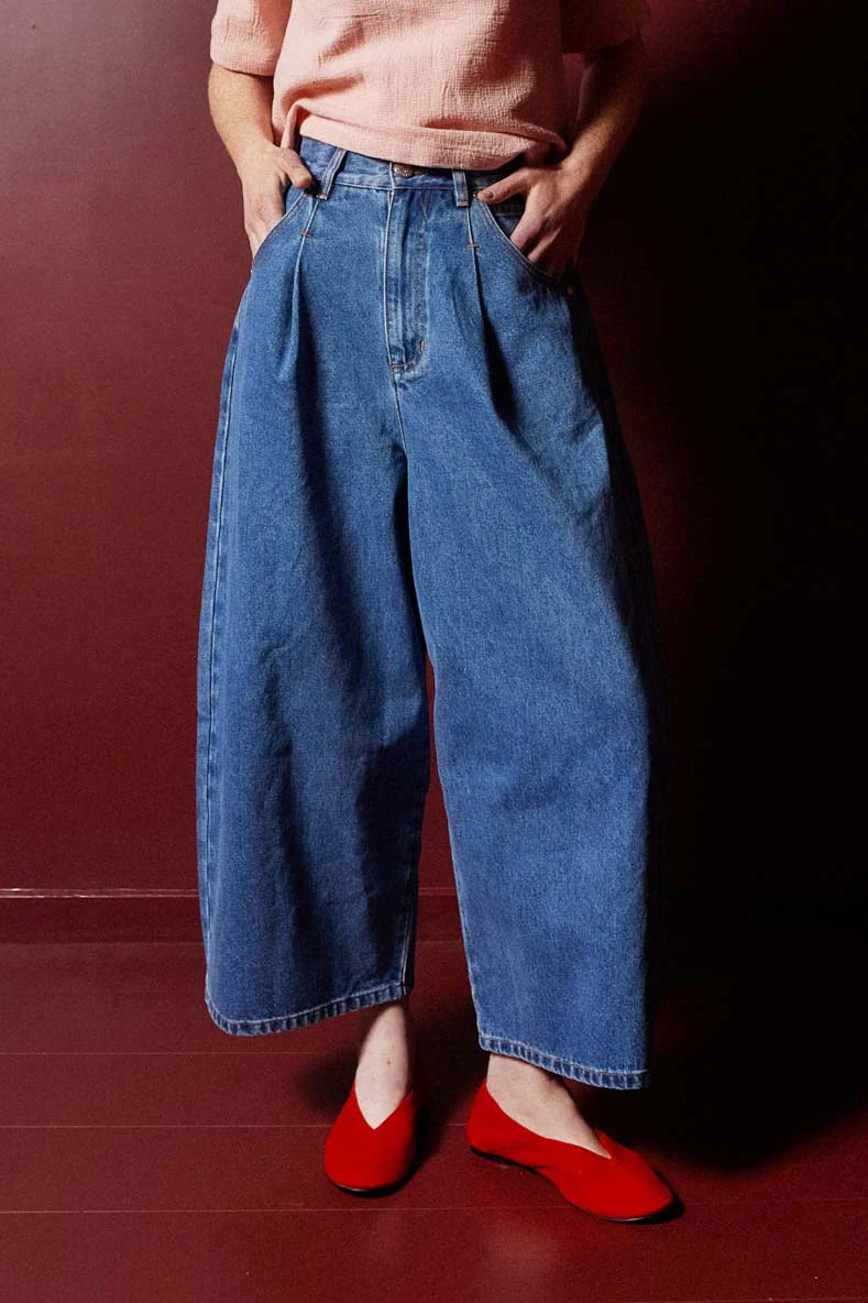 Person wearing blue jeans and red shoes against a dark background