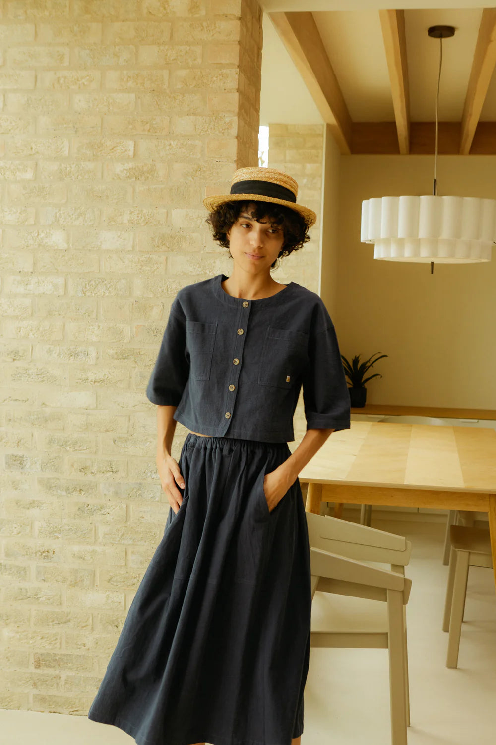 Woman in a navy matching shirt and top standing in a room with a textured wall and a dining table.