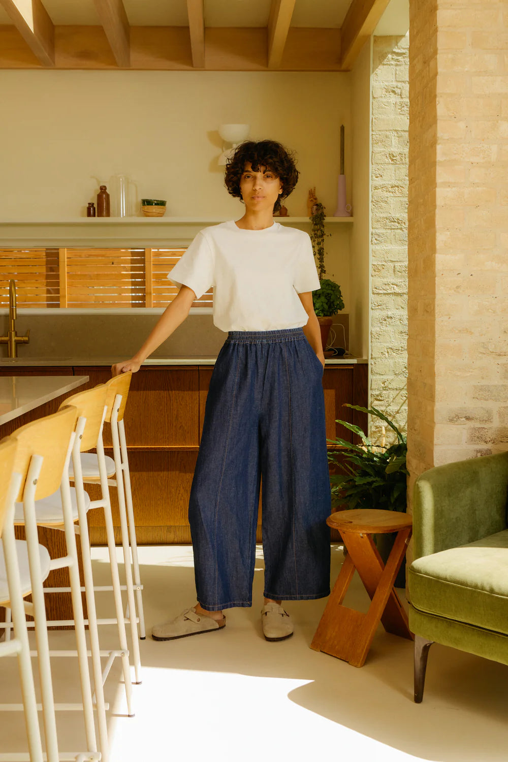 Person wearing LF Markey Denim trousers standing in a modern kitchen with white walls and wooden accents