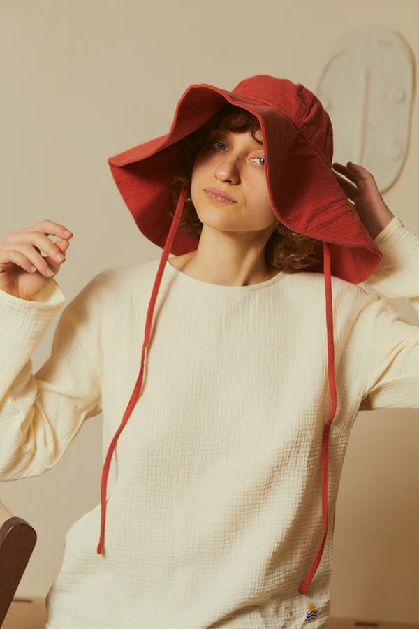 Person wearing a soft red LF Markey sun hat and white sweater indoors