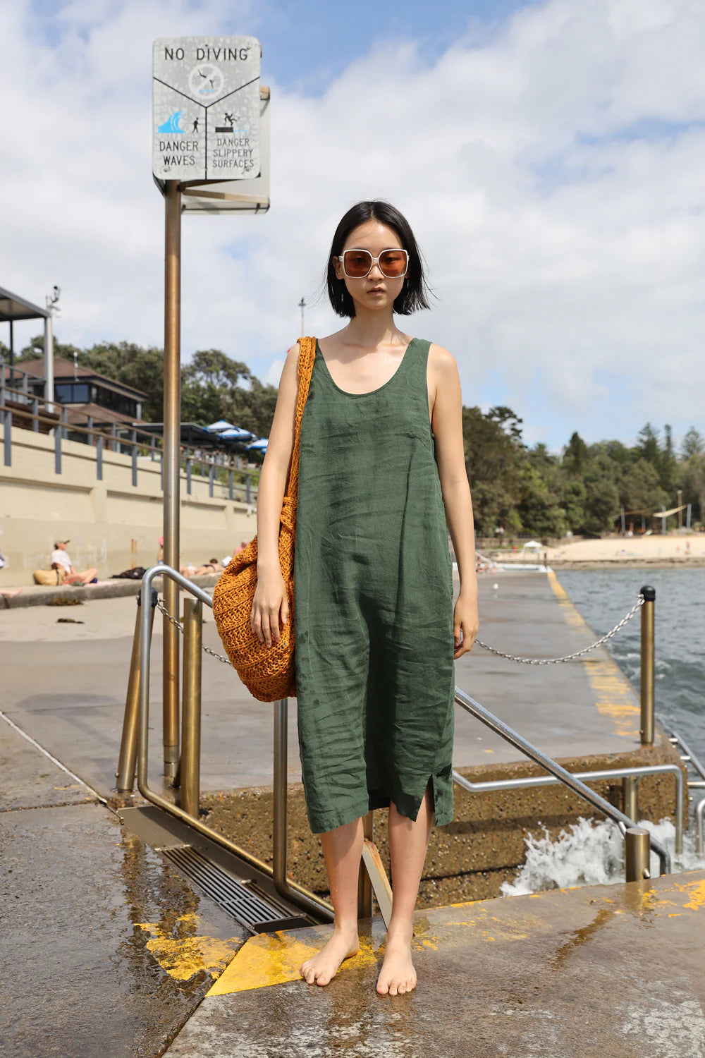 Woman in a green LF Markey dress standing on a dock with a beach in the background