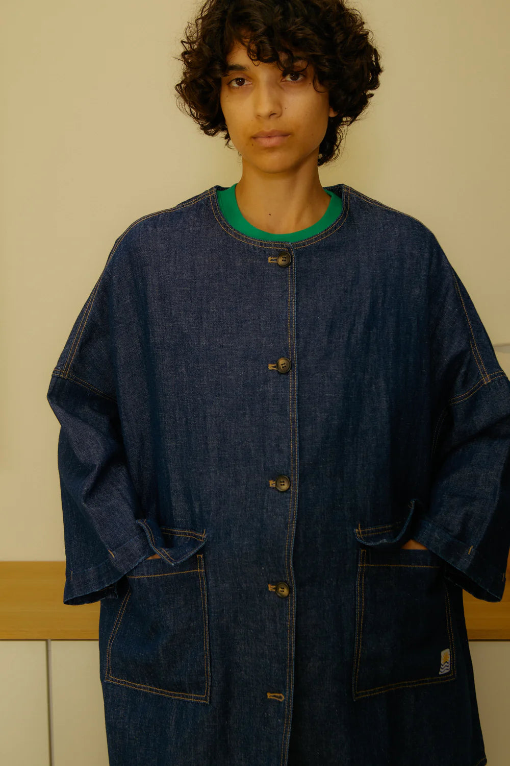 Person wearing a blue denim coat over a green shirt against a neutral background