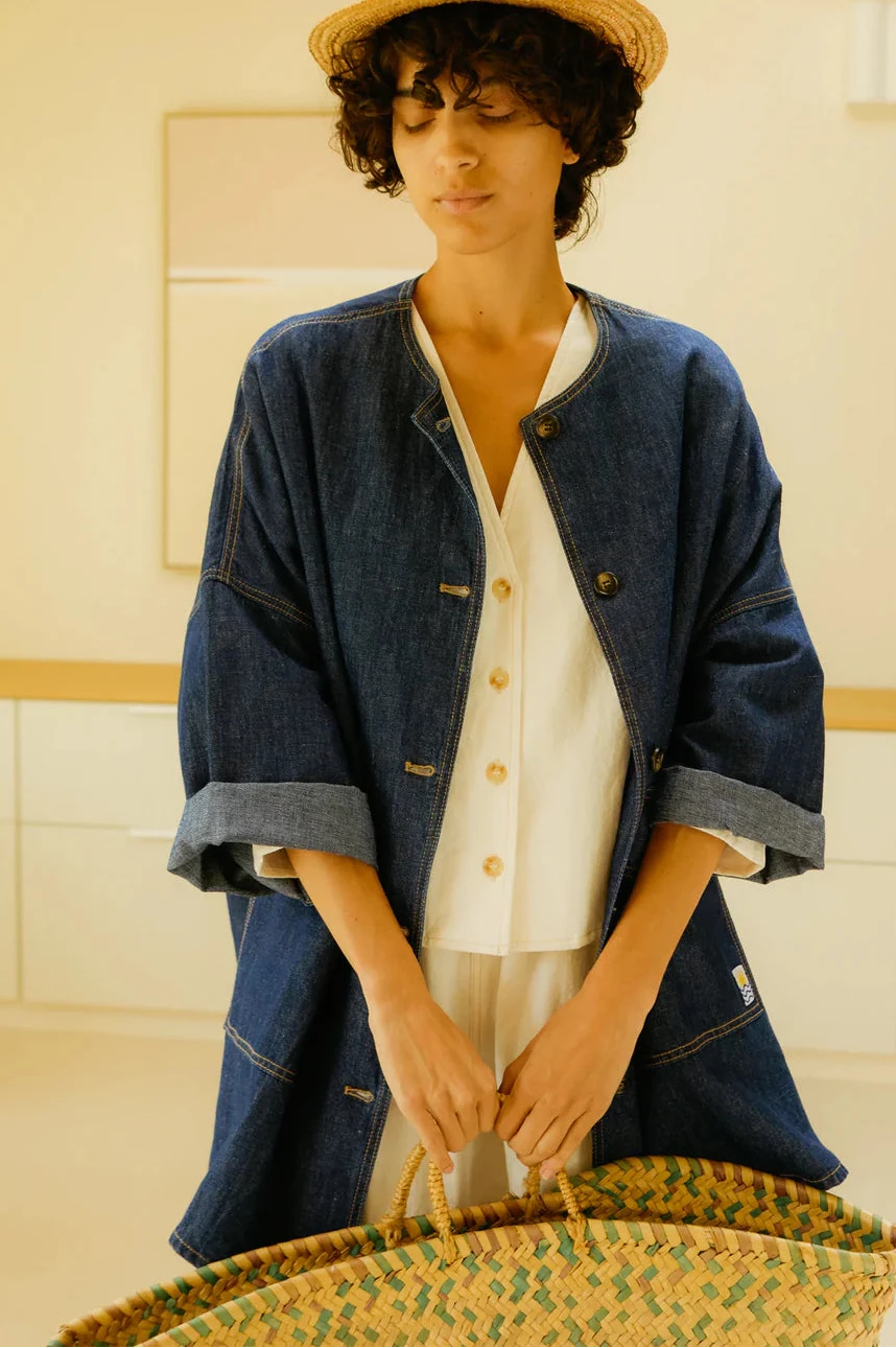Person wearing a blue jacket and straw hat in a room with wooden beams.