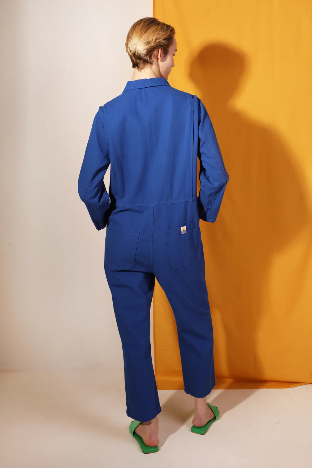 Person wearing a blue LF Markey jumpsuit standing against a yellow wall.