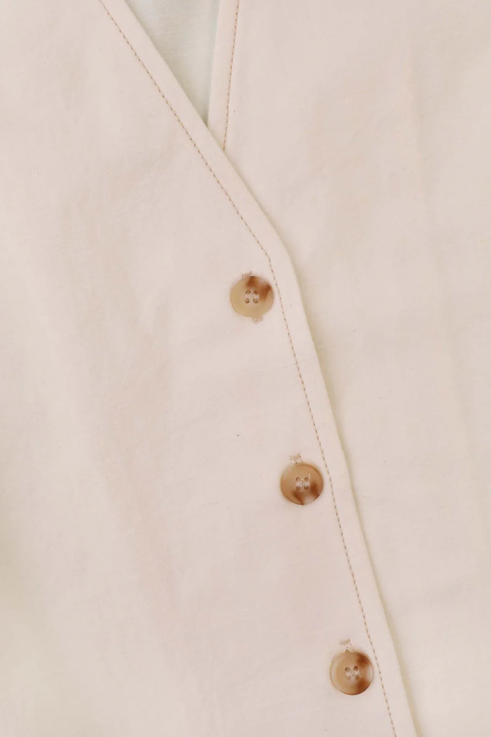 Close up view of ecru LF Markey top with tortoiseshell button detail and contrasting stitching 