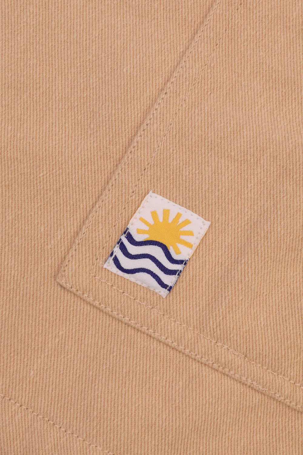 Close-up of a label with a sun and wave design on beige fabric.