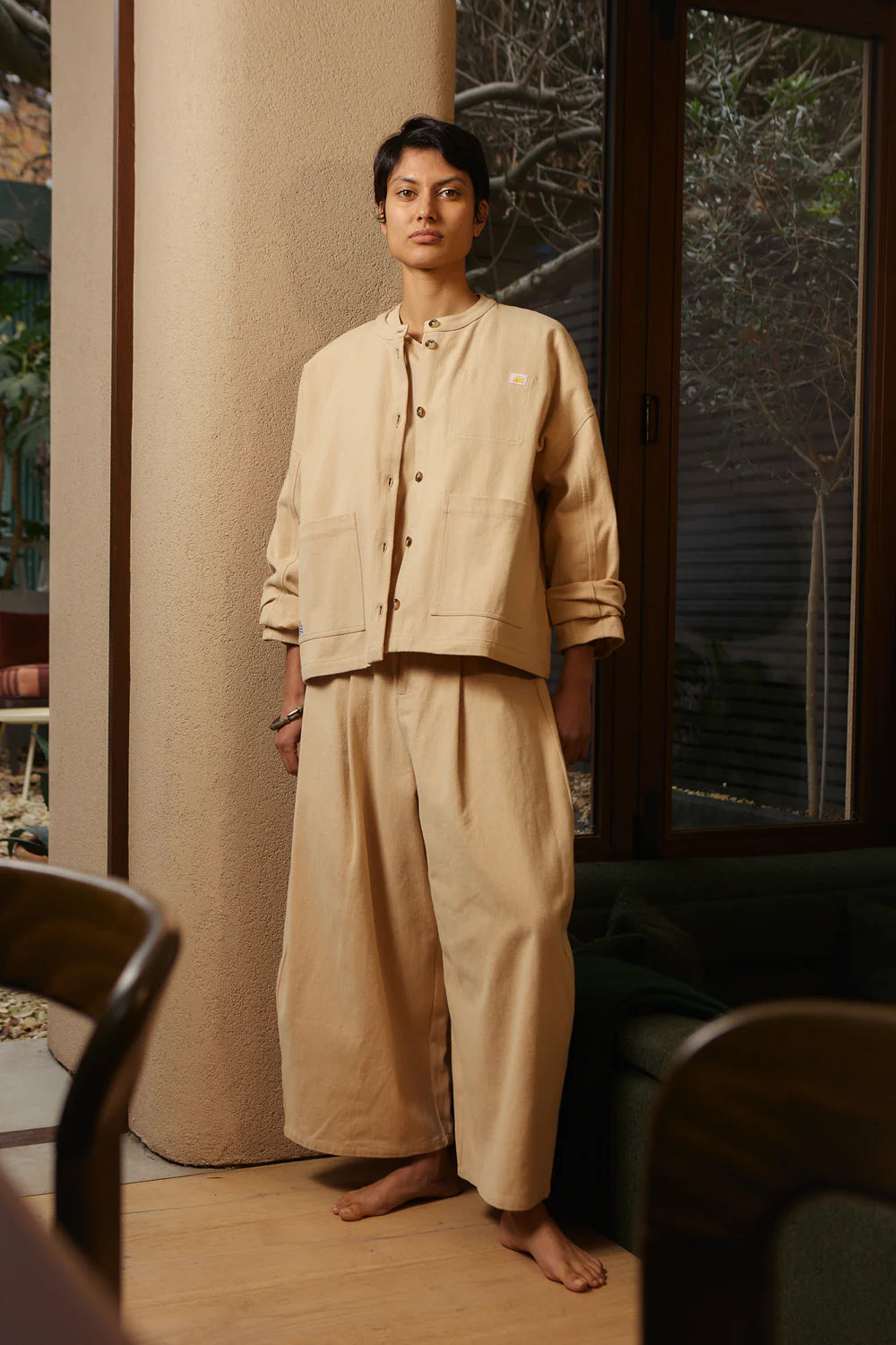 Person wearing a beige LF Markey Jacket and trousers standing in a room with a window in the background