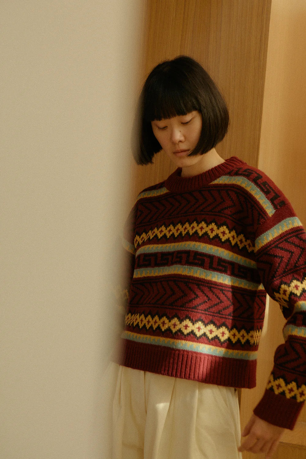 Person wearing a patterned LF Markey sweater standing against a neutral wall.