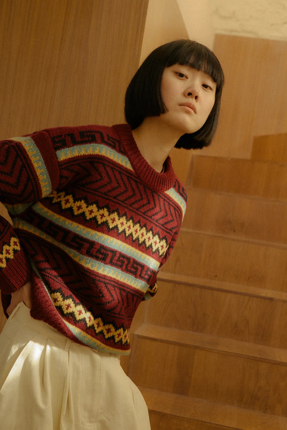 Person wearing a patterned sweater standing on wooden stairs