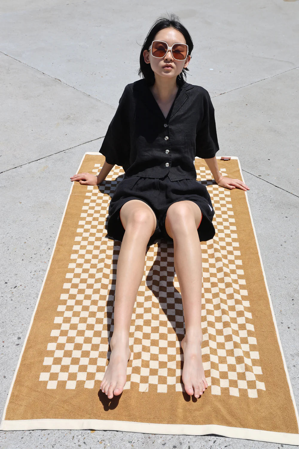 Woman sitting on a large checkered towel outdoors wearing matching Black lf Markey shirt and shorts set 