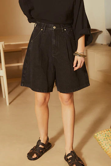 Person wearing black denim shorts and sandals indoors.