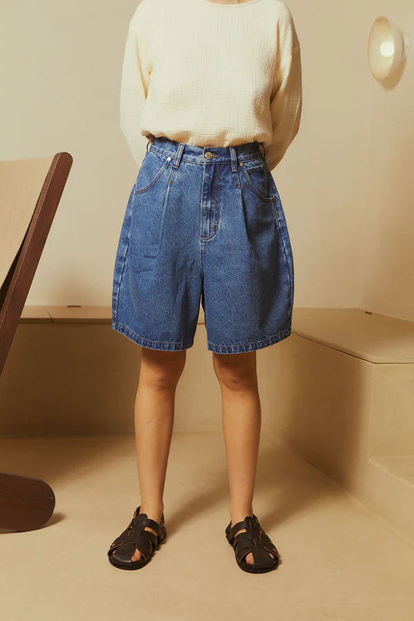 Person wearing blue denim shorts and a cream sweater in a minimal indoor setting.