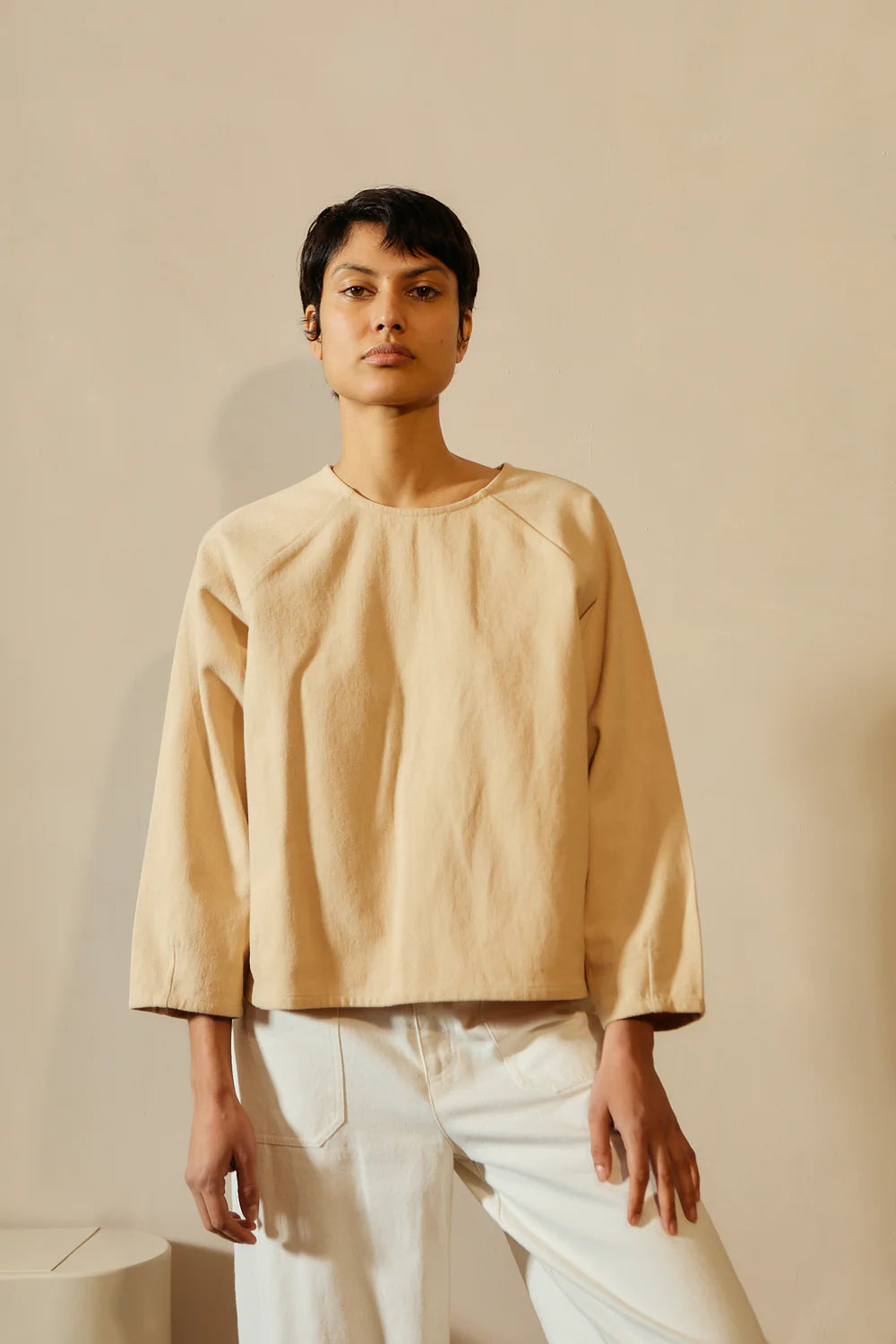 Person wearing a beige top and white pants against a beige background