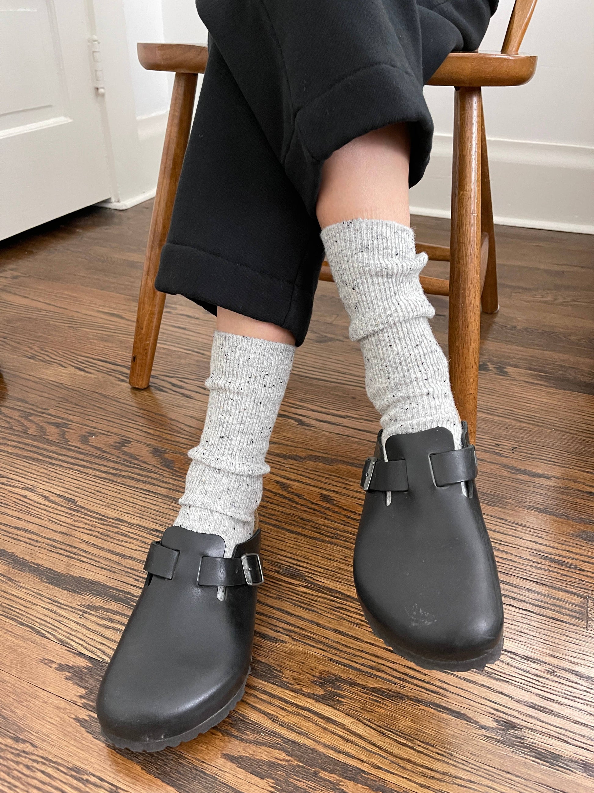 Person wearing black clogs and grey  Le Bon Shoppe socks on a wooden floor.