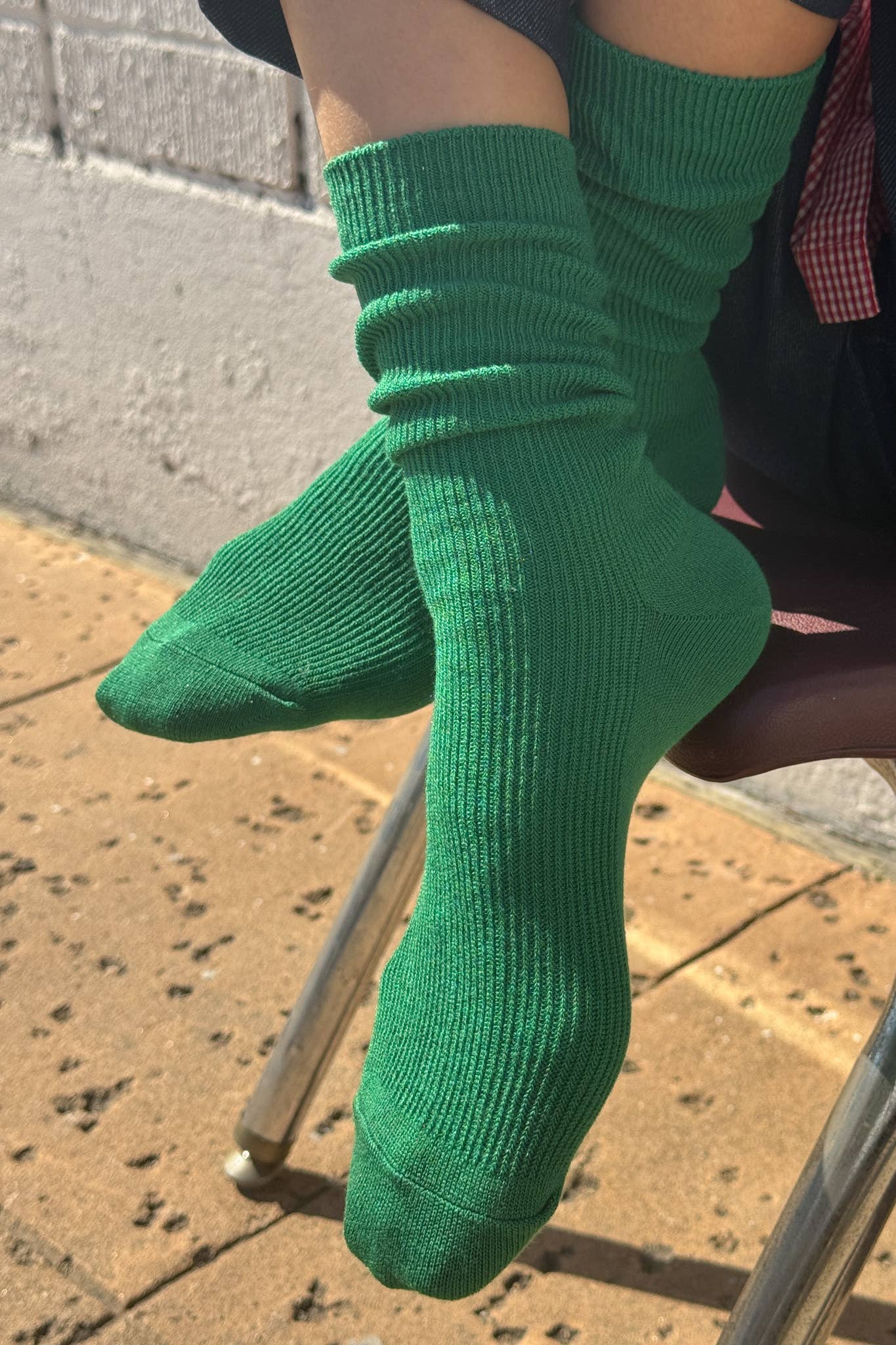 Green Le Bon Shoppe socks being worn on a person sitting on a chair with a brick wall background
