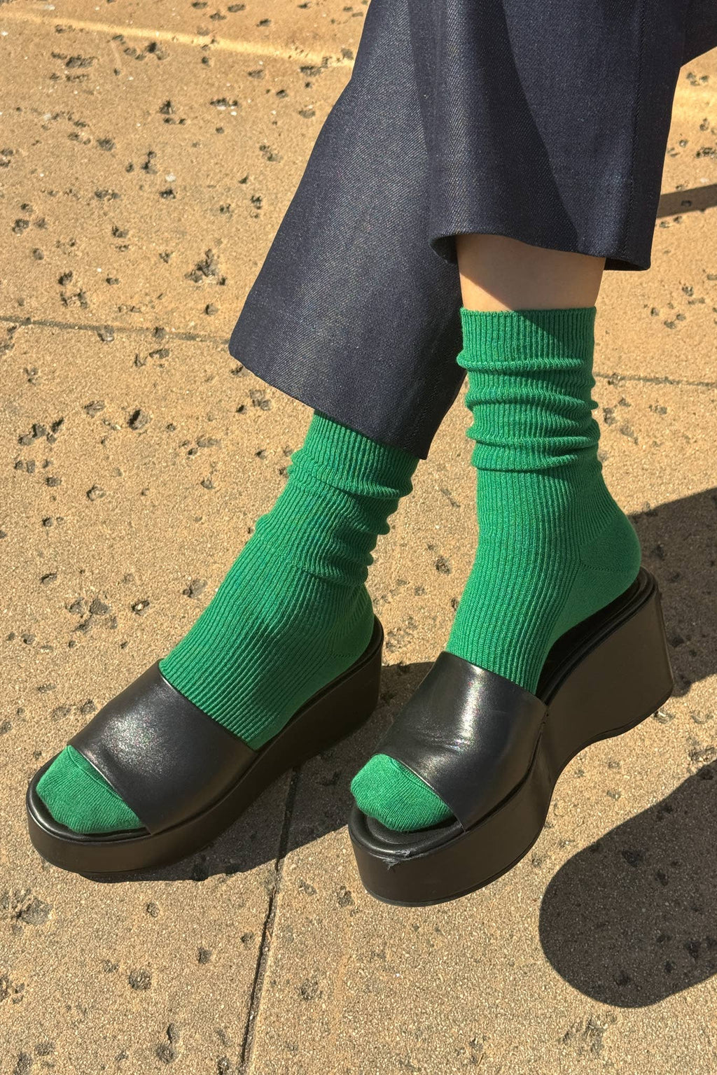 Green Le Bon Shoppe socks worn with black platform shoes on a textured pavement.