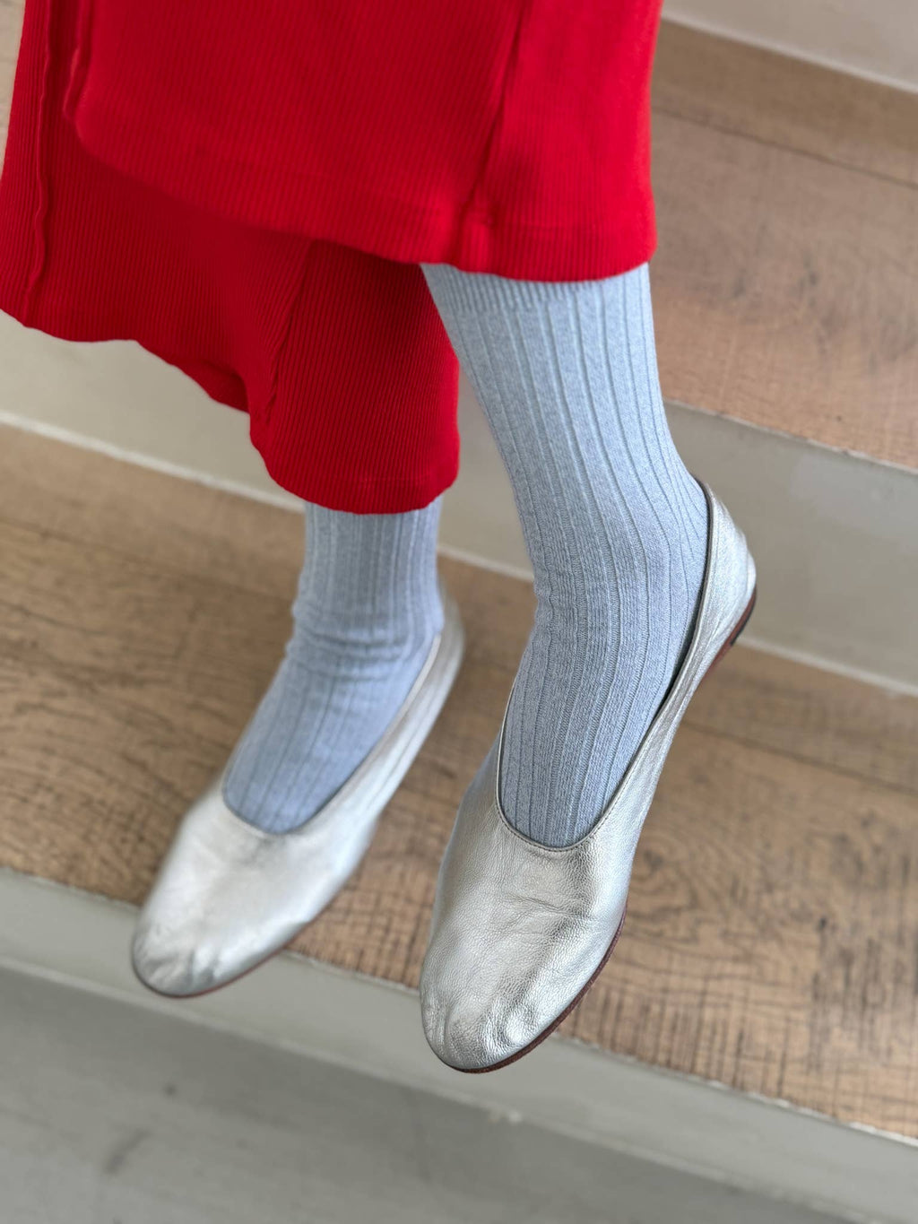 Person wearing red trousers, blight blue Le Bon Shoppe  socks, and silver flats on a wooden floor.