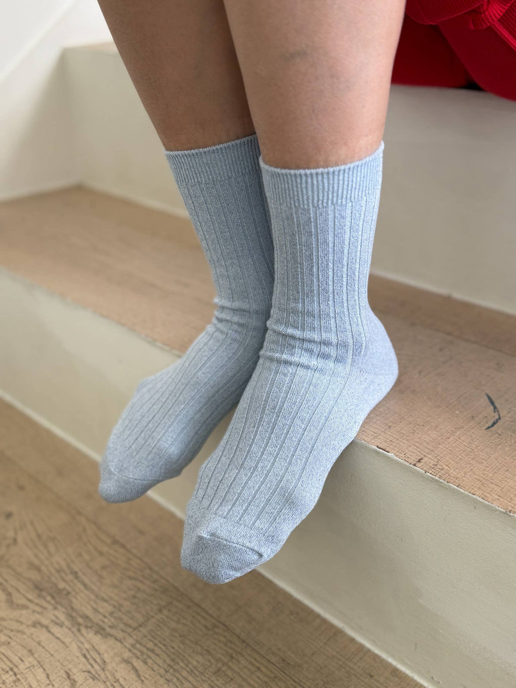 Light blue Le Bon Shoppe socks worn by a person sitting on a wooden floor.