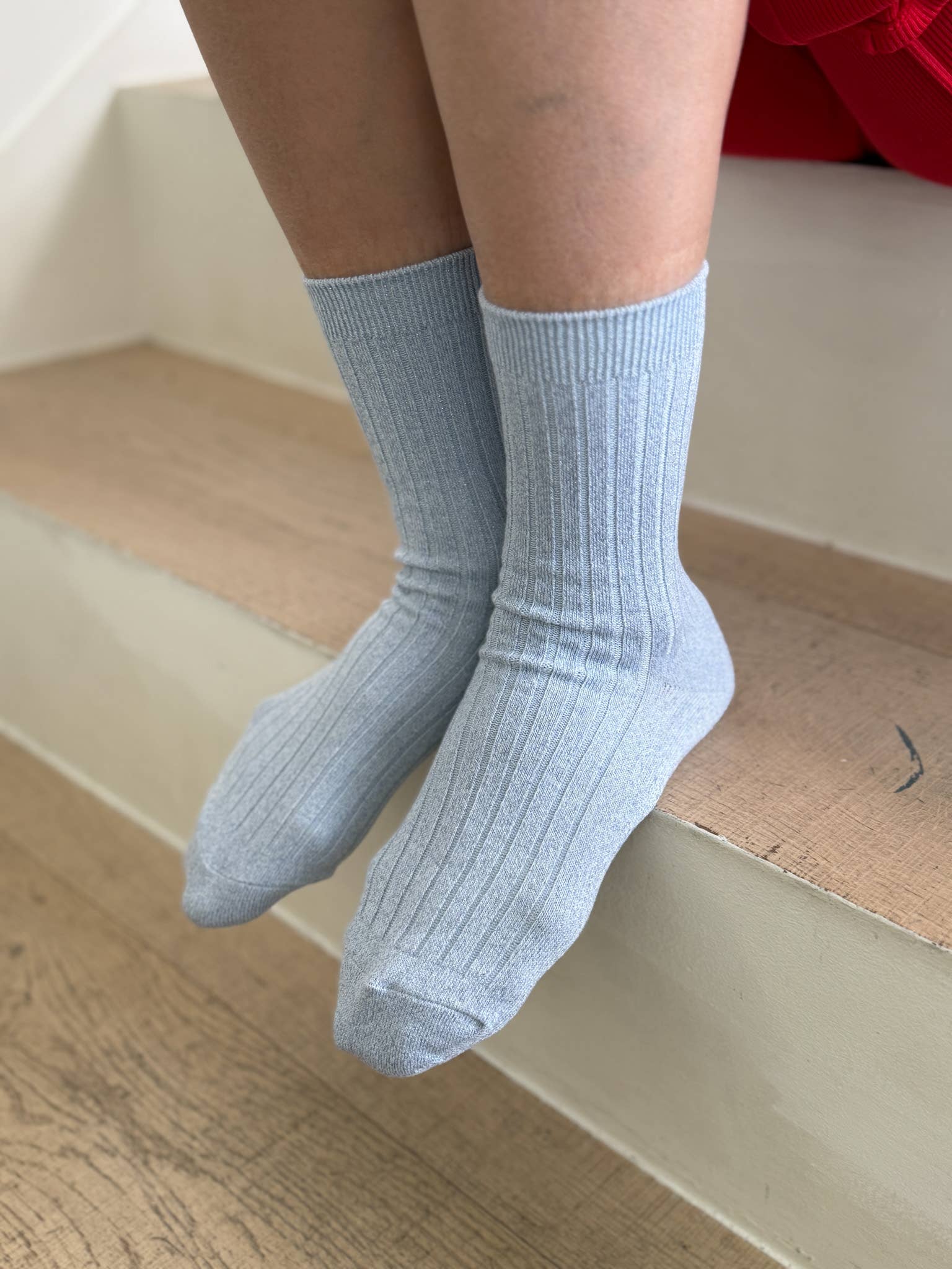 Light blue Le Bon Shoppe socks worn by a person sitting on a wooden floor.