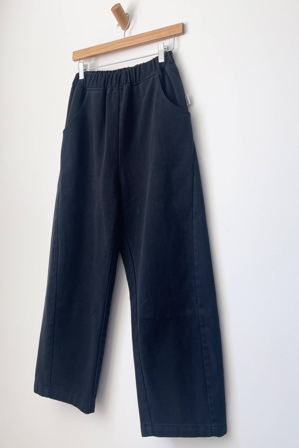 Navy blue Le Bon Shoppe Arc pants hanging on a wooden hanger against a white background