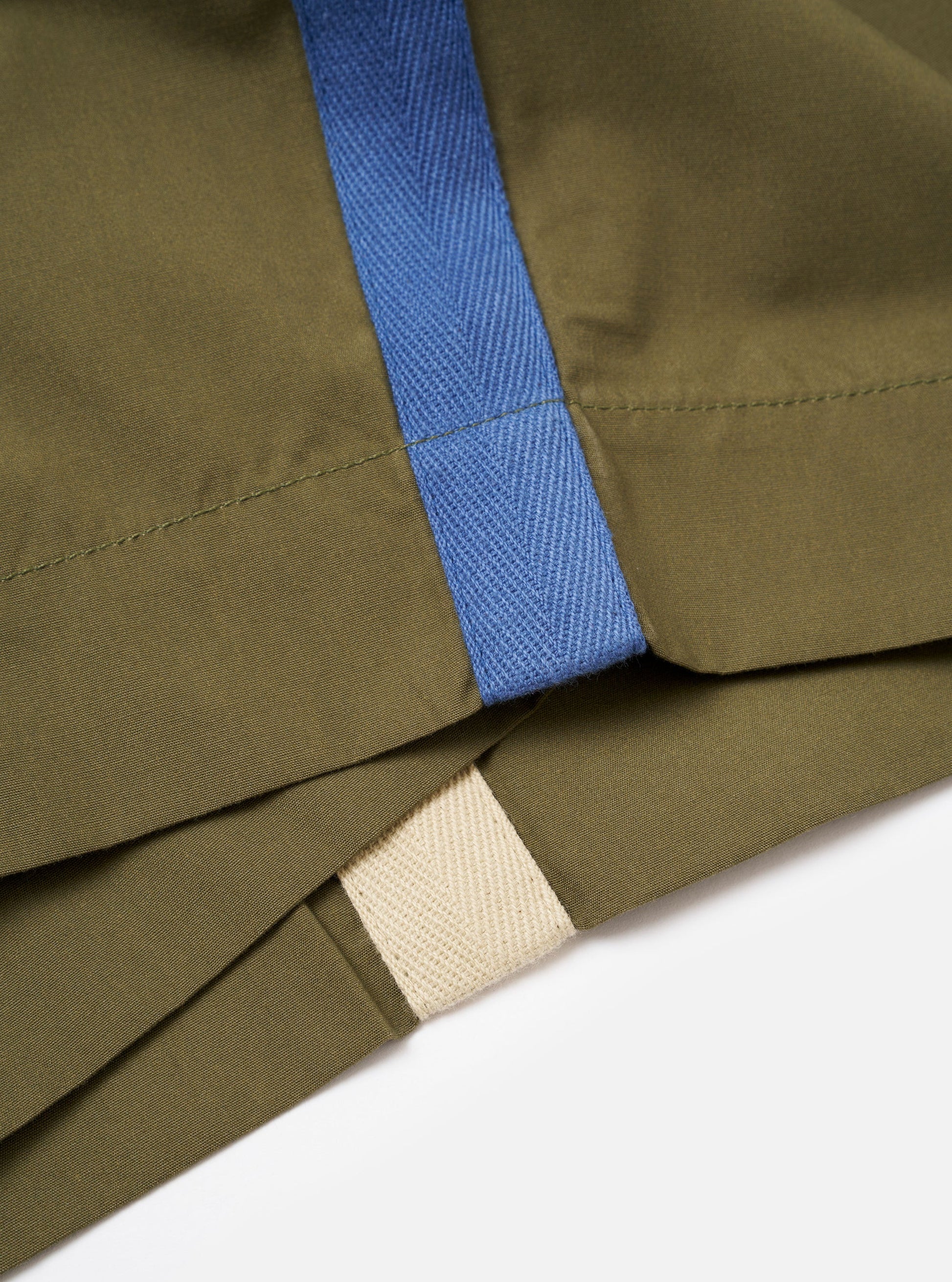Close-up of green fabric with blue and beige trim on a white background