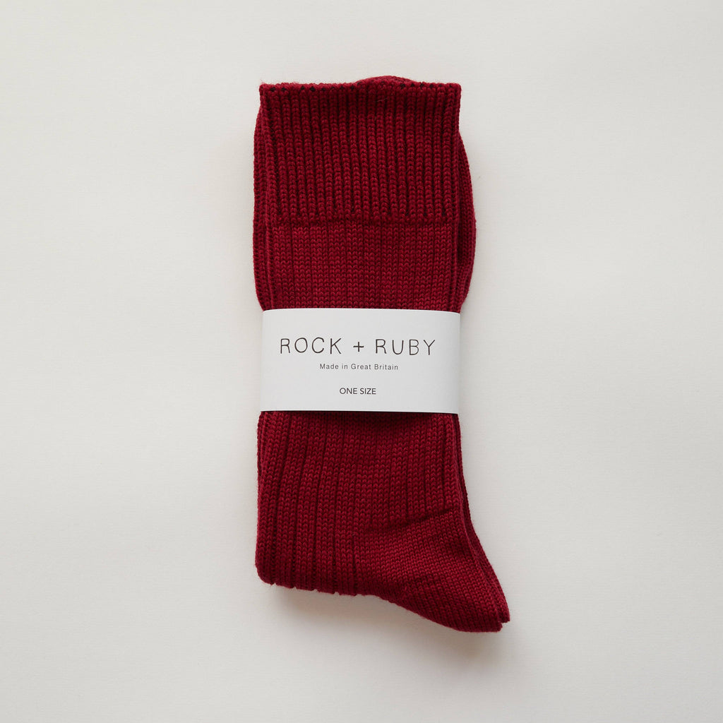 Pair of red socks with a 'Rock + Ruby' label on a light gray background