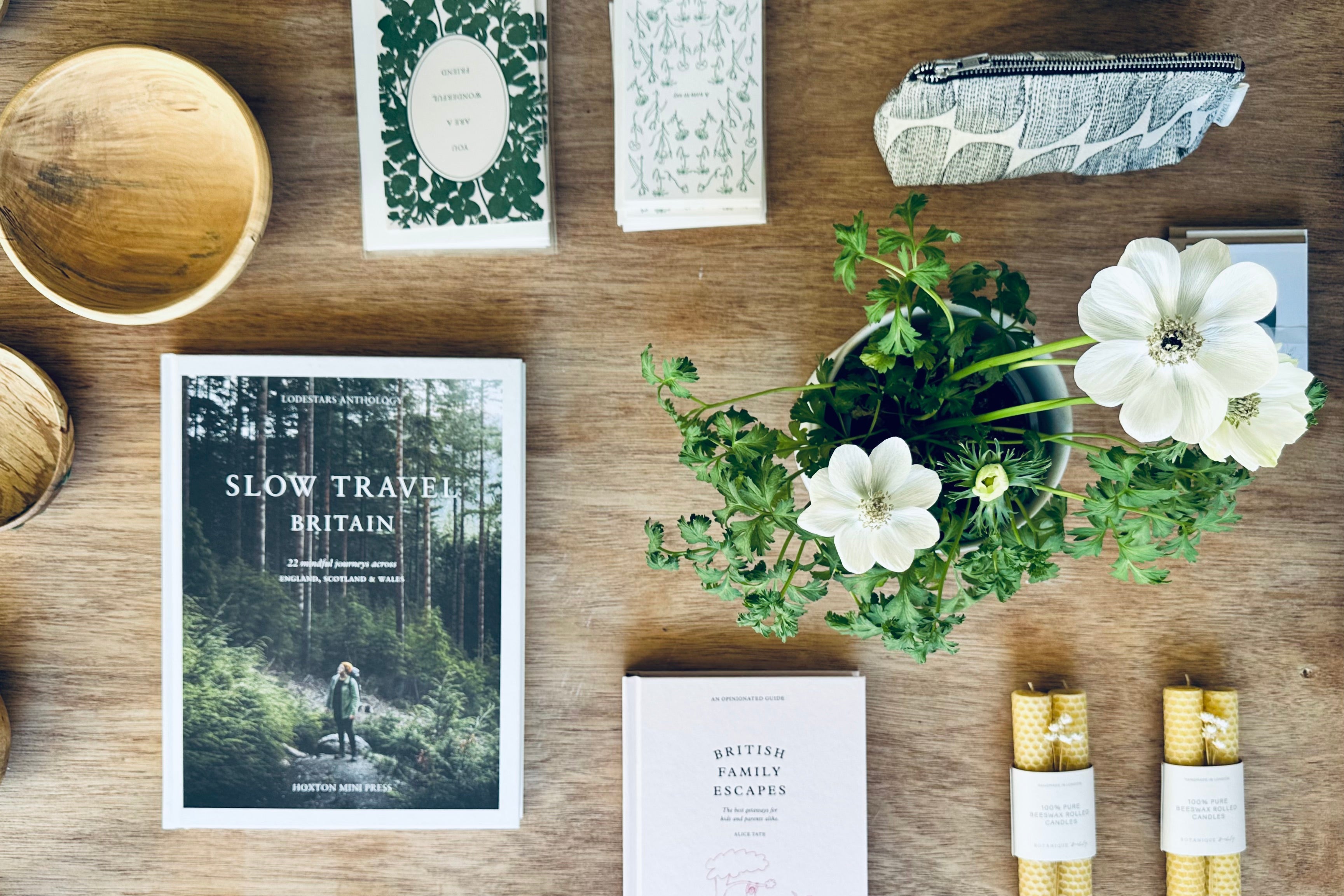 Tabletop scene with 'Slow Travel Britain' book, candles, and plants on a wooden surface