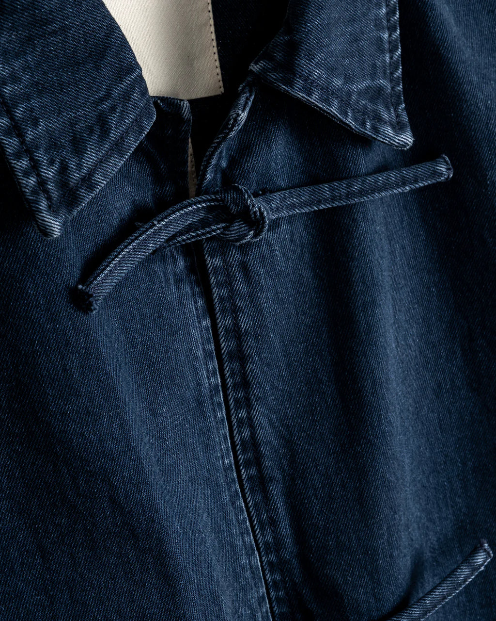 Close-up of a navy denim jacket with a tie detail.