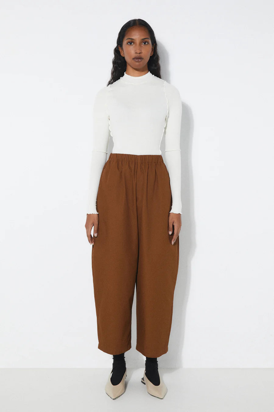 Woman wearing a white turtleneck and Rita Rowtobacco high-waisted pants on a white background