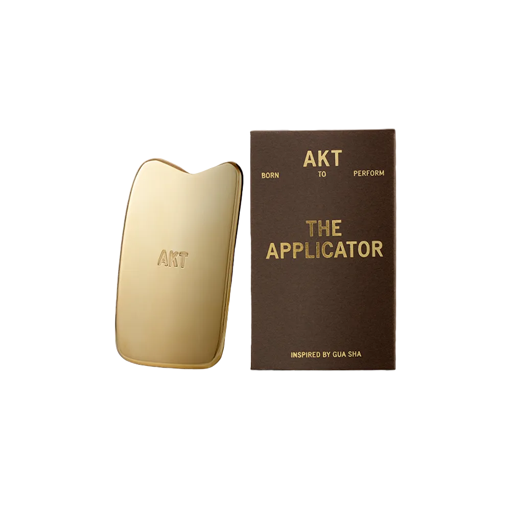 Gold applicator and brown box with 'AKT' branding on a beige background
