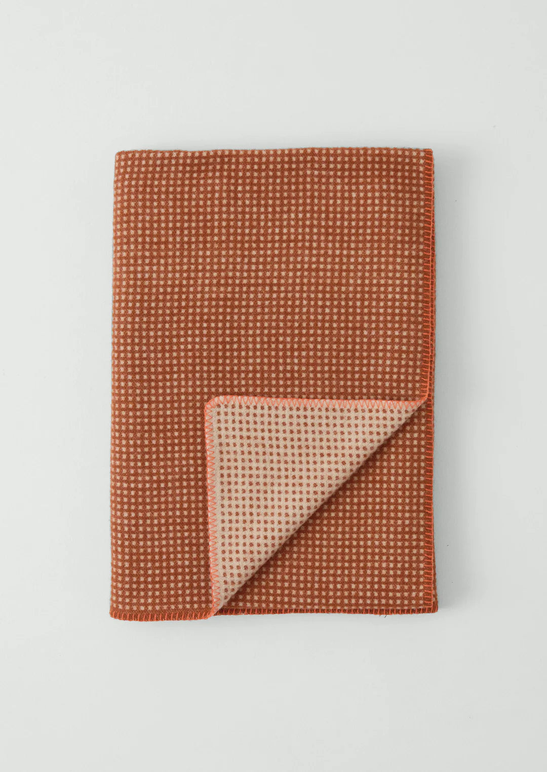 Rust textured blanket with a beige corner on a light gray background