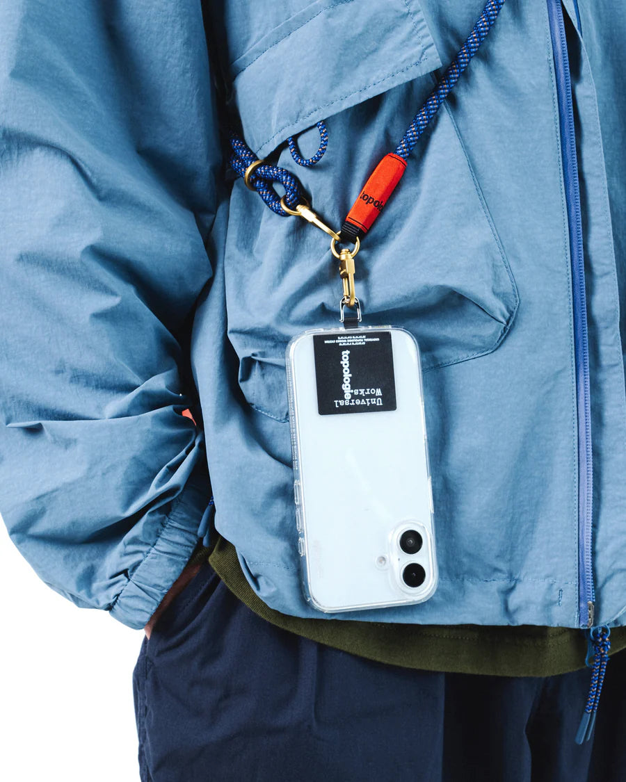 Blue Topogloie phone strap with a white phone case with black label against  a blue jacket