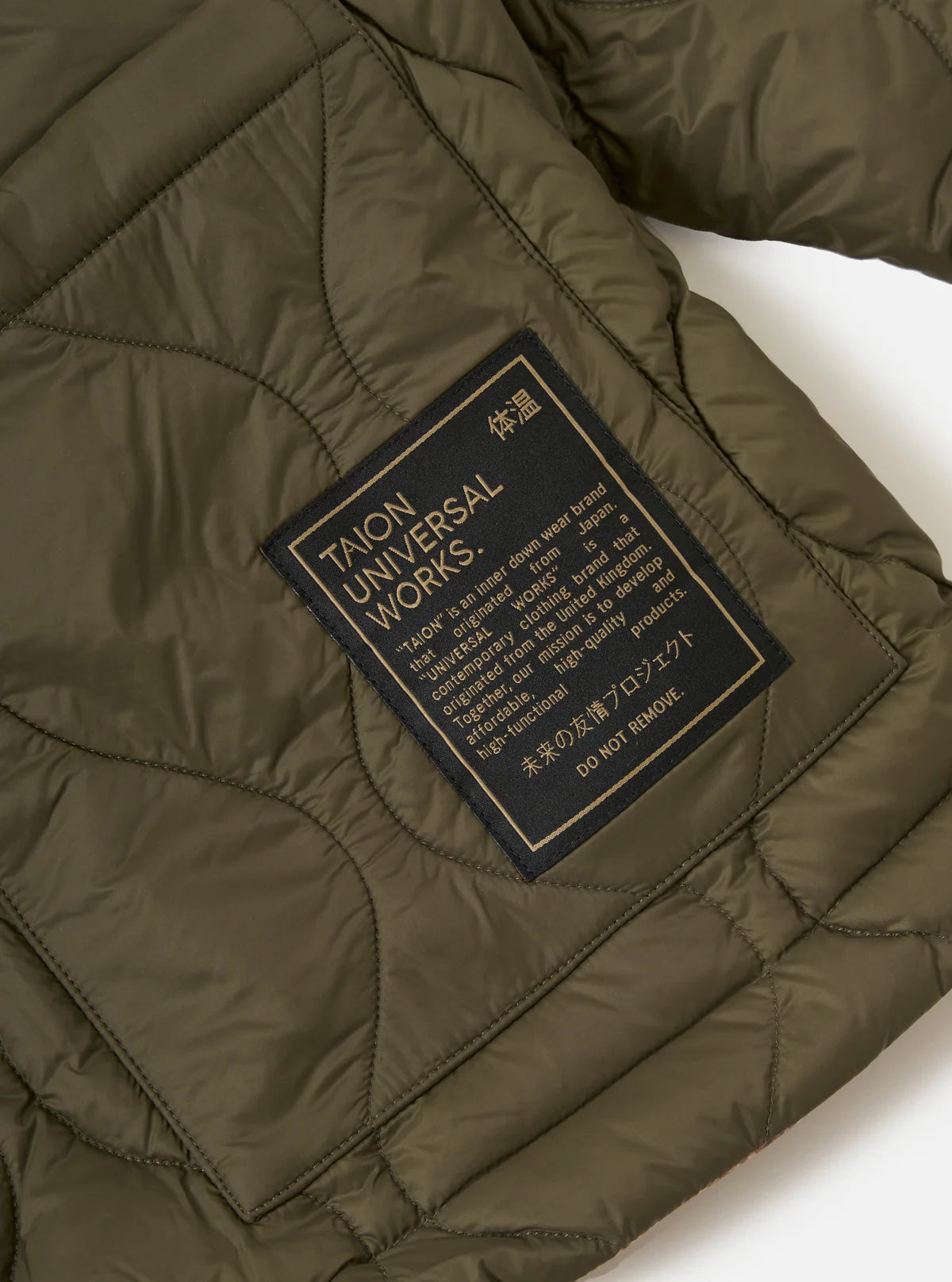 Close-up of a quilted jacket with a Taion and Universal Works label on a white background