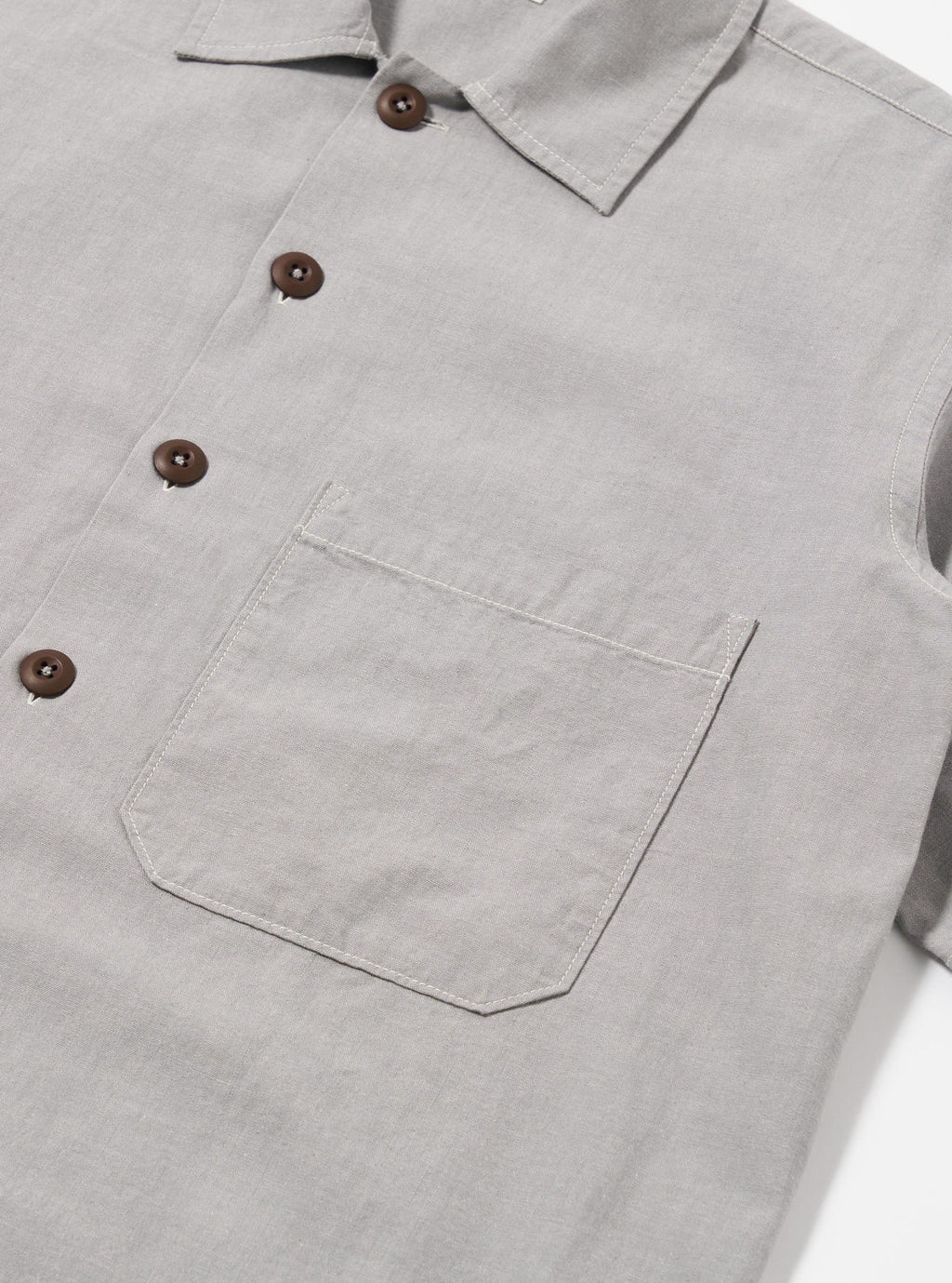 Close-up of a light gray shirt with brown buttons and a pocket on a white background