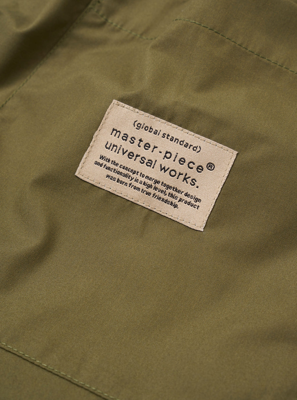 Universal Works and masterpiece label on a green fabric surface with text