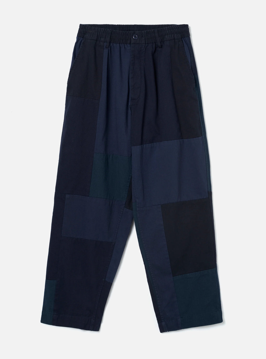 A pair of Universal Works patchwork trousers in dark navy and navy, featuring an elastic waistband and a relaxed, cropped silhouette, shown against a light gray background.