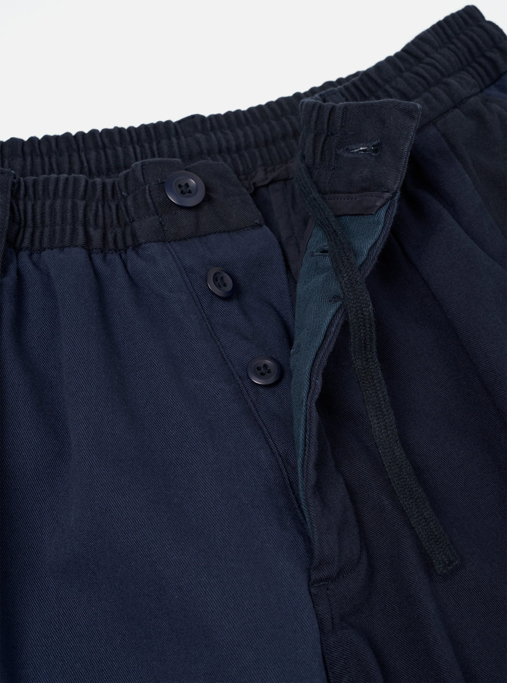 Universal Works Navy Twill patchwork Oxford pant close up fly detail against a light grey background. 
