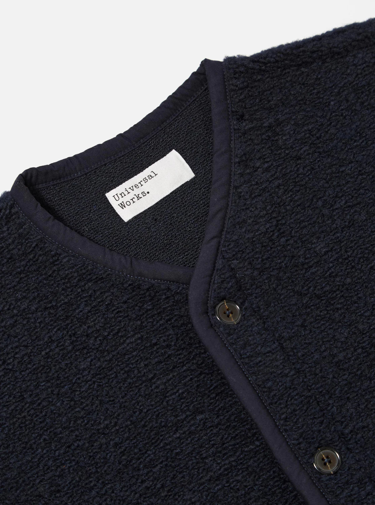 Navy textured Universal Works navy gilet with a visible brand label on a light gray background