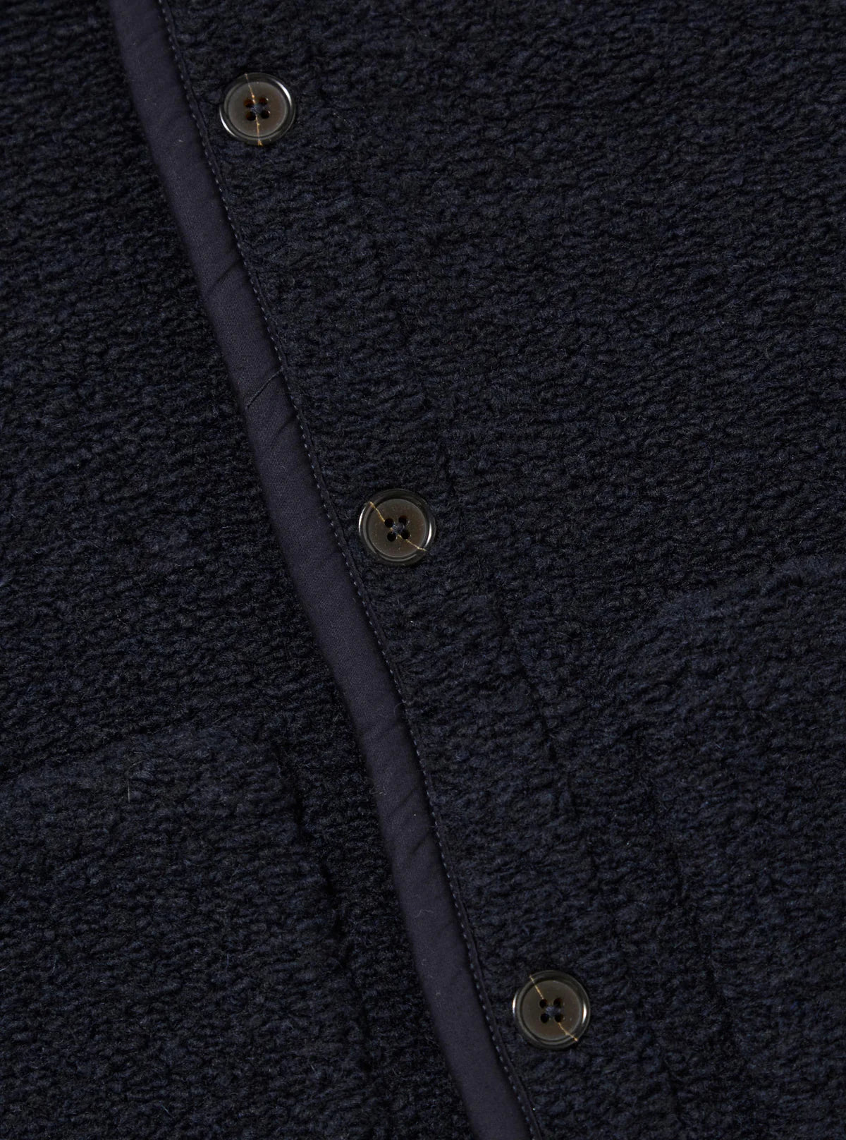 Close-up of a textured Universal Works navy wool fleece with buttons and a seam.