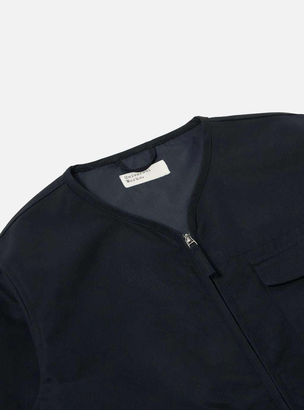 Universal Works navy  jacket with a label on a light grey background