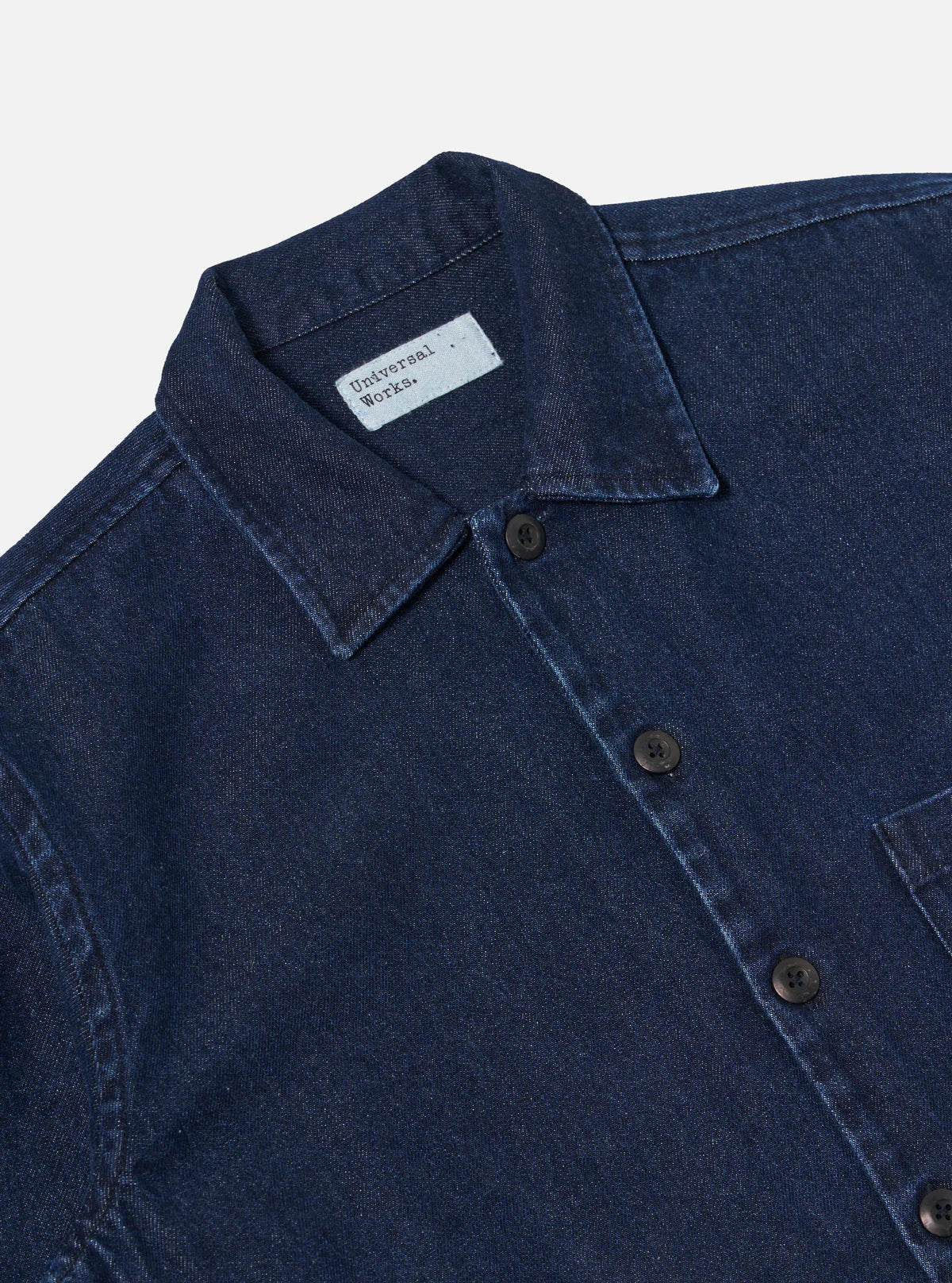 Close-up of Universal Works blue denim shirt with collar and buttons on a light gray background