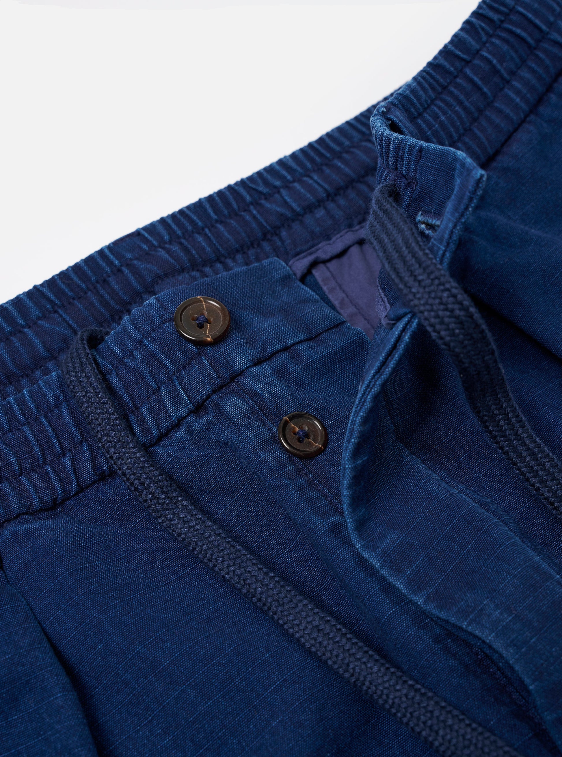 Detail of buttons and waist drawstring of the Universal Works indigo kimstop pleated track pant 