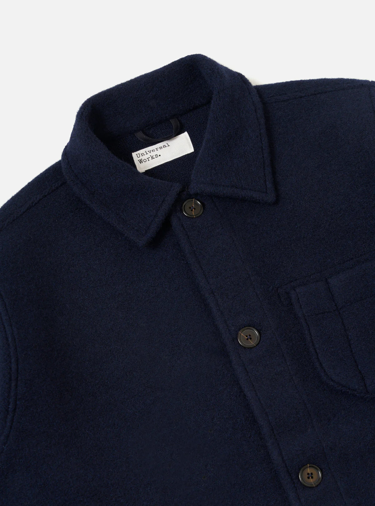 Universal Works navy blue coat with a collar and buttons, featuring a brand label on a light grey background.