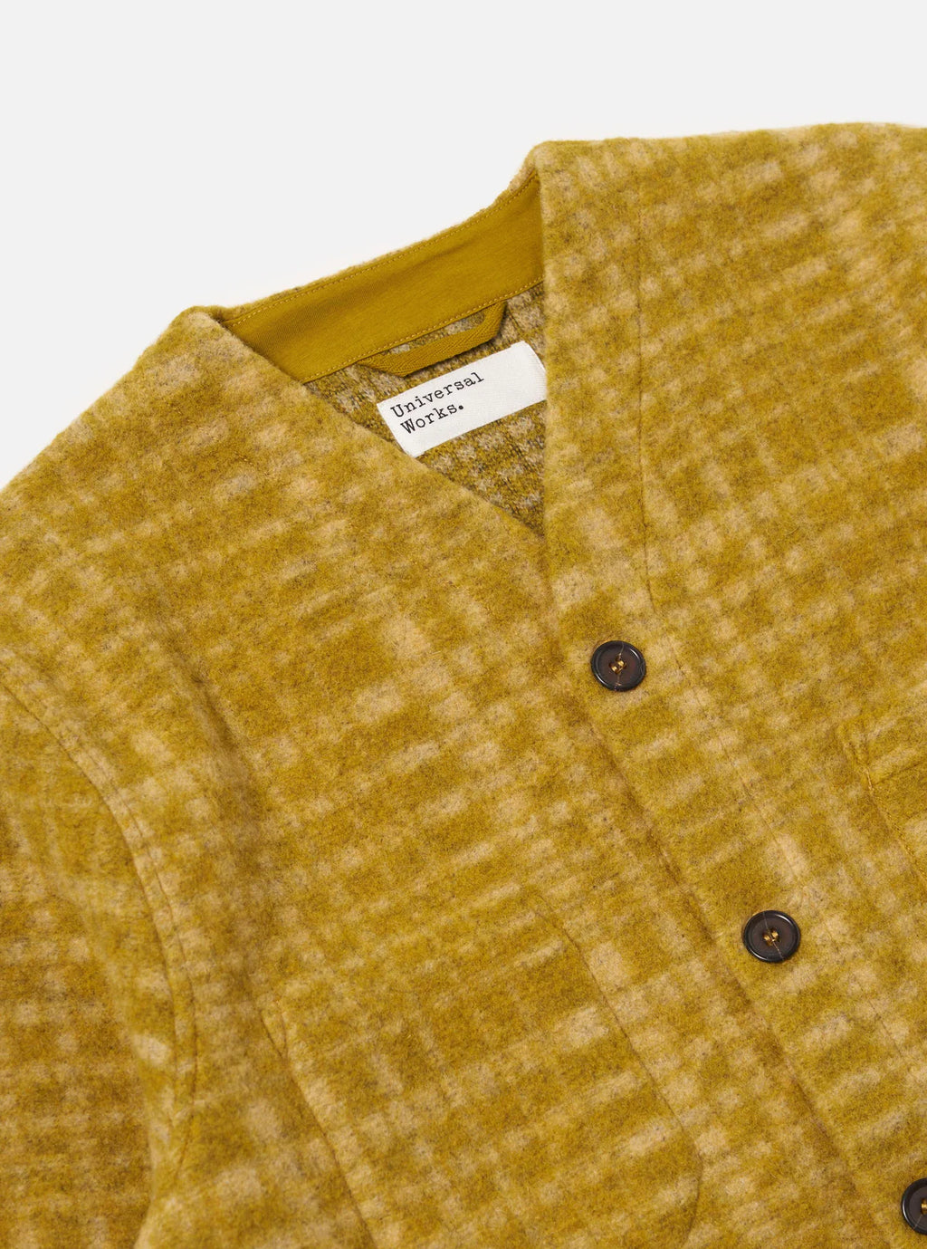 Close-up of a mustard yellow textured jacket with a Universal Works label on a light gray background