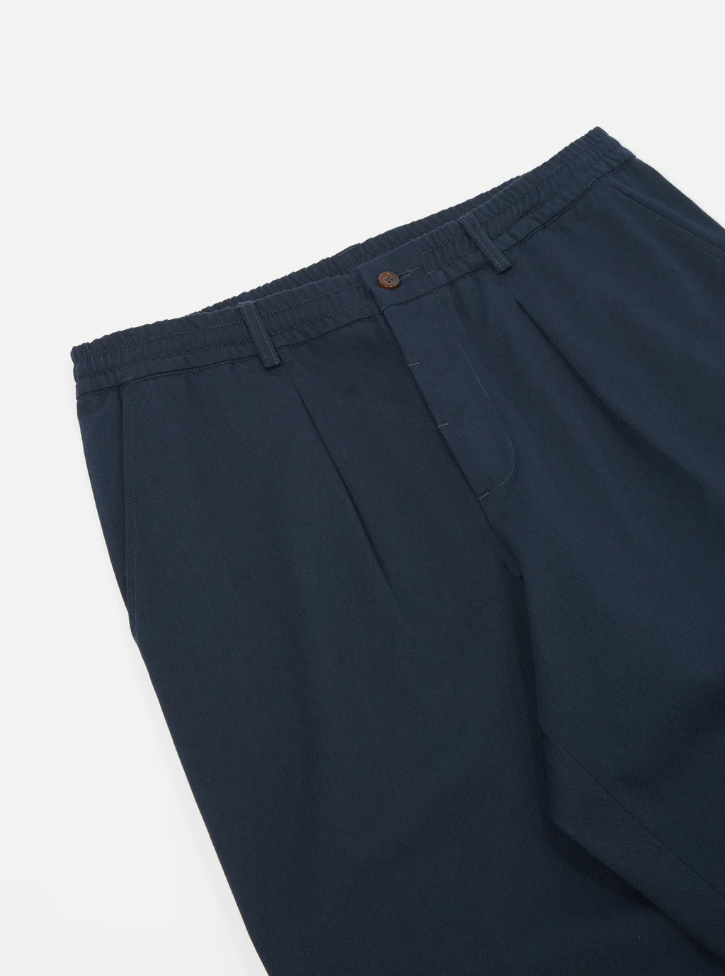 Universal Works navy pleated pants on a light grey background